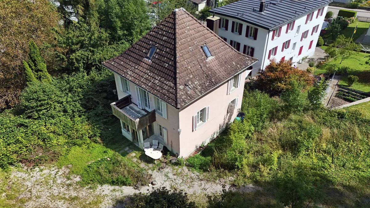 Man sieht ein Einfamilienhaus mit kleinem Balkon und verwildertem Garten.